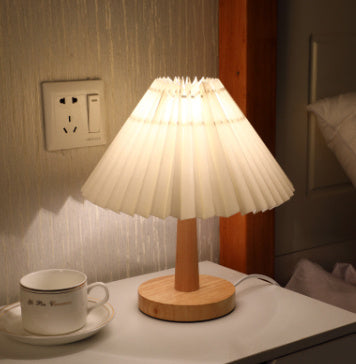 Pleated-shade table lamp lit warm beside a teacup on a nightstand