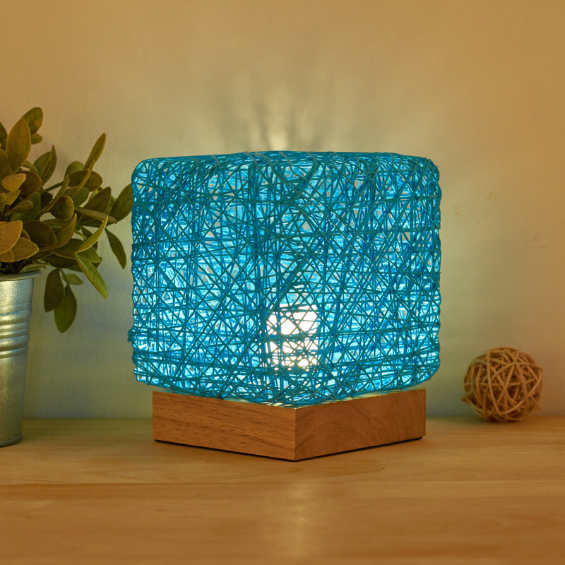 Blue woven rattan table lamp lit on a wooden base