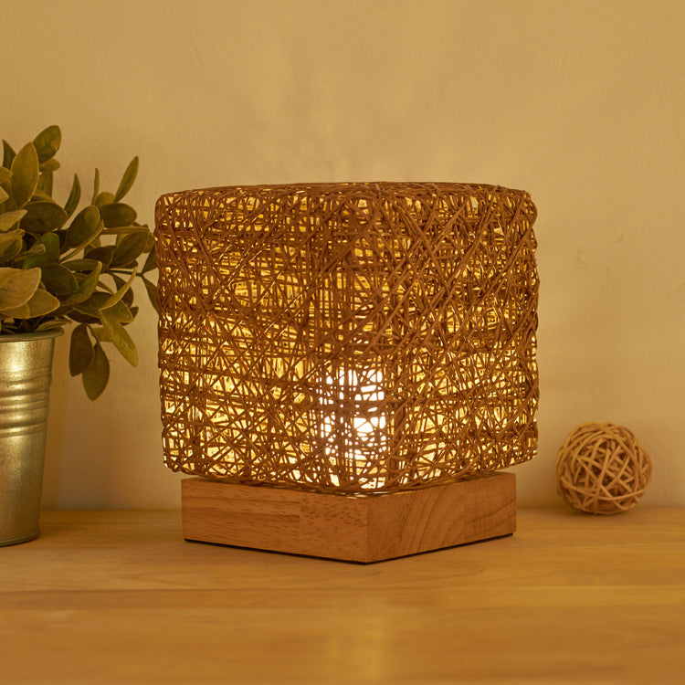 Gold-brown woven rattan table lamp lit on a wooden base
