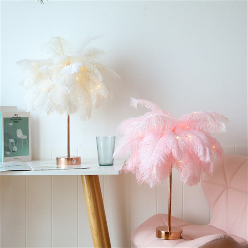 Pink feather table lamp lit on a console table beside a vase