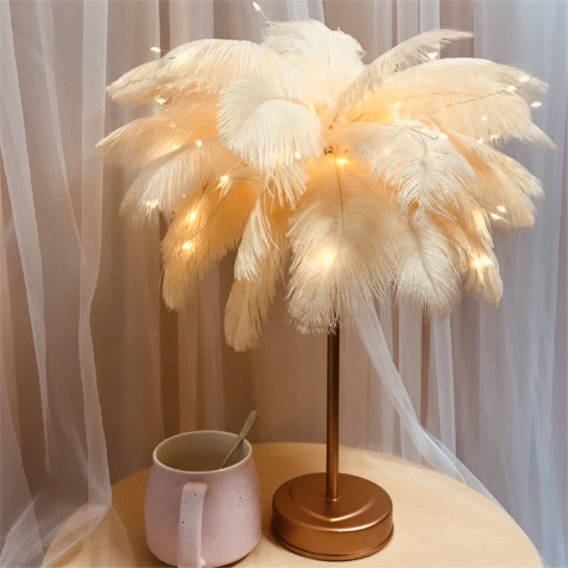 White feather table lamp lit on a gold base, sheer curtain behind