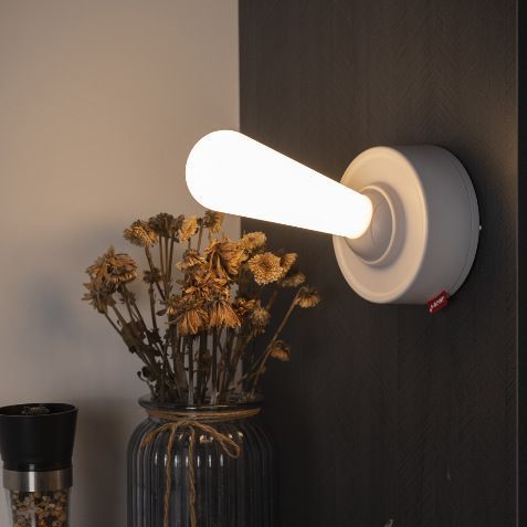 Cordless silicone wall light mounted on a dark wall above dried flowers