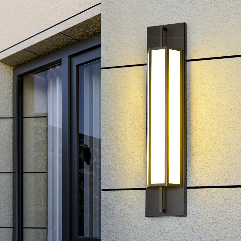 Outdoor wall sconce lit warm on a rendered house wall beside a window