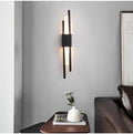 Black linear wall sconce lit above a side table beside a sofa