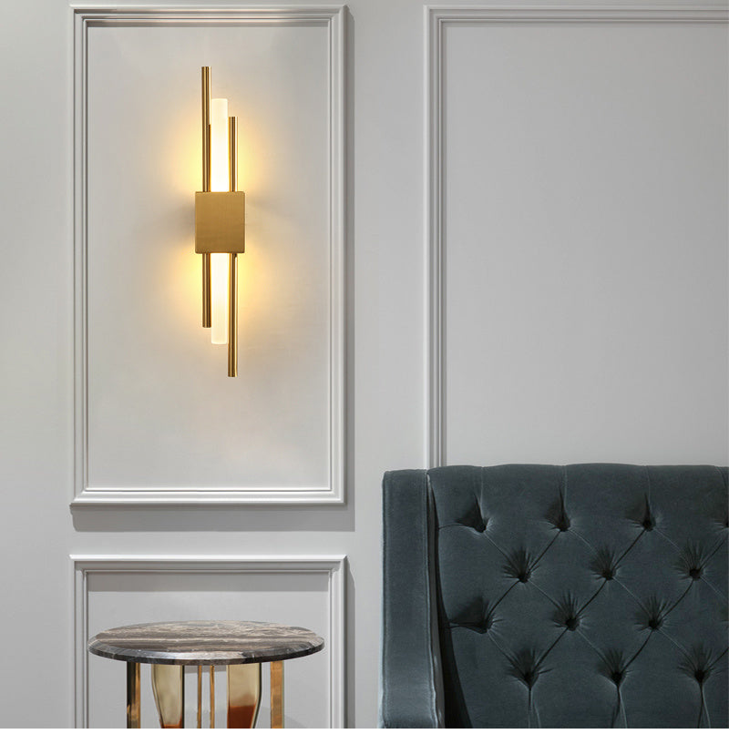 Gold linear wall sconce lit on a panelled wall beside an armchair