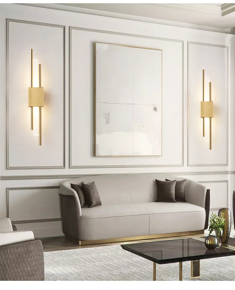 Two gold linear wall sconces lit either side of artwork in a living room