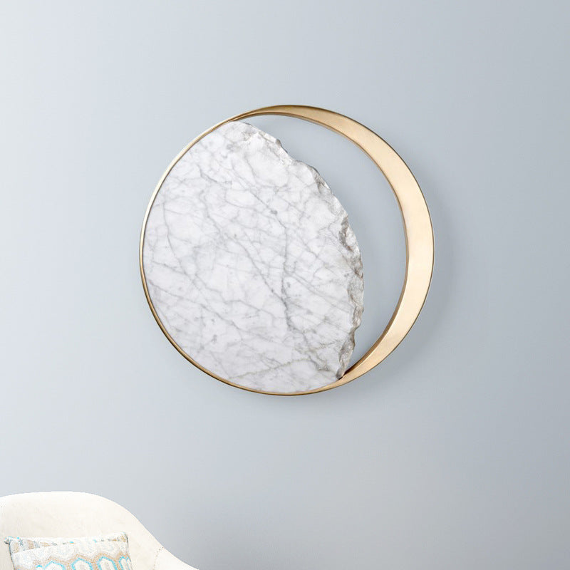 Round marble and gold wall sconce lit on a pale wall