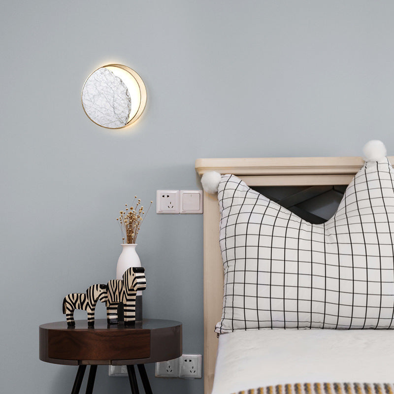 Round marble and gold wall sconce lit above a bedside table