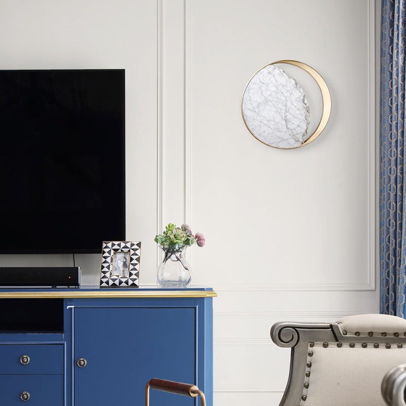 Round marble and gold wall sconce mounted beside a television
