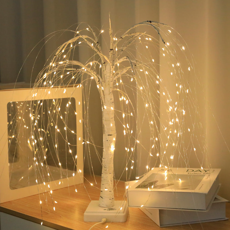 LED willow tree light lit beside a picture frame on a bedside table